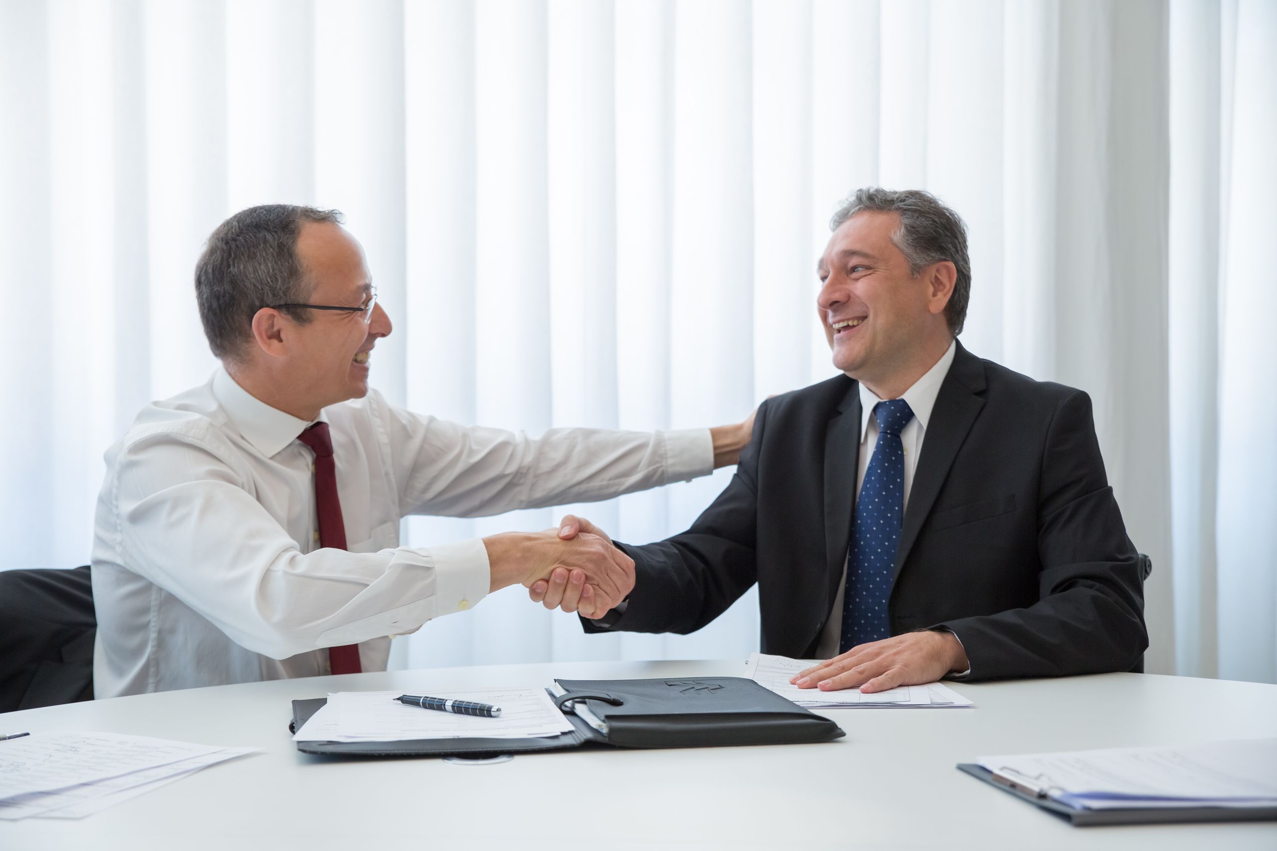 Two businessmen in a bright office seal a deal with a handshake, conveying agreement and cooperation.